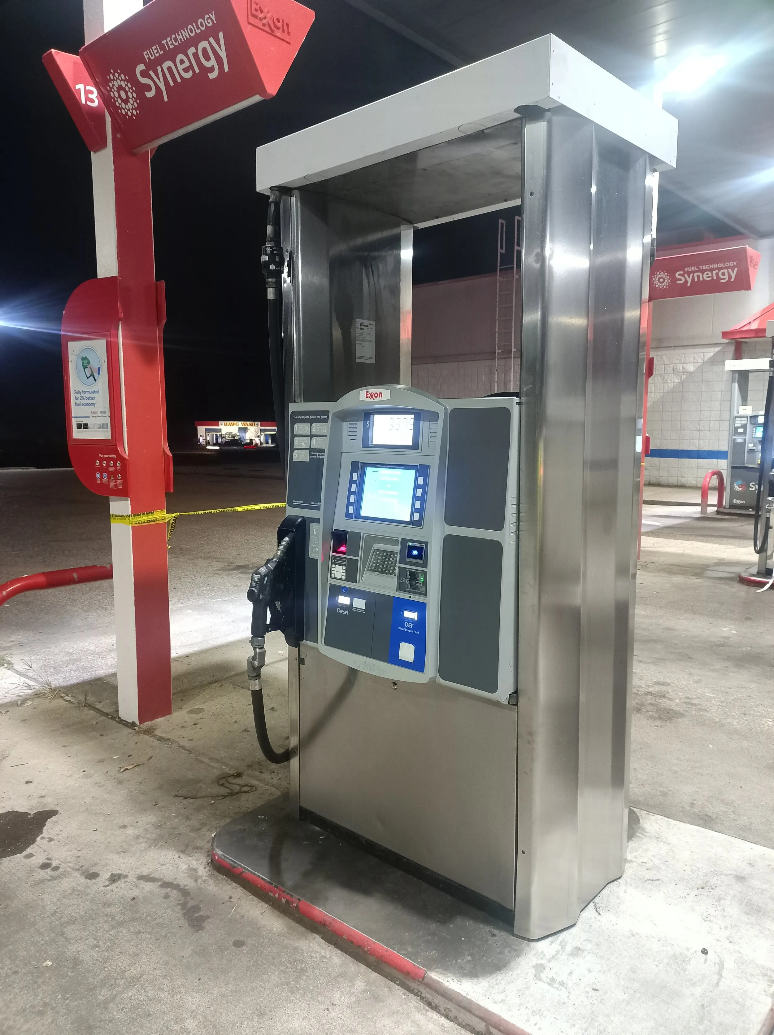 A stainless steel fuel dispenser being serviced at night under a lit forecourt canopy at a branded station.