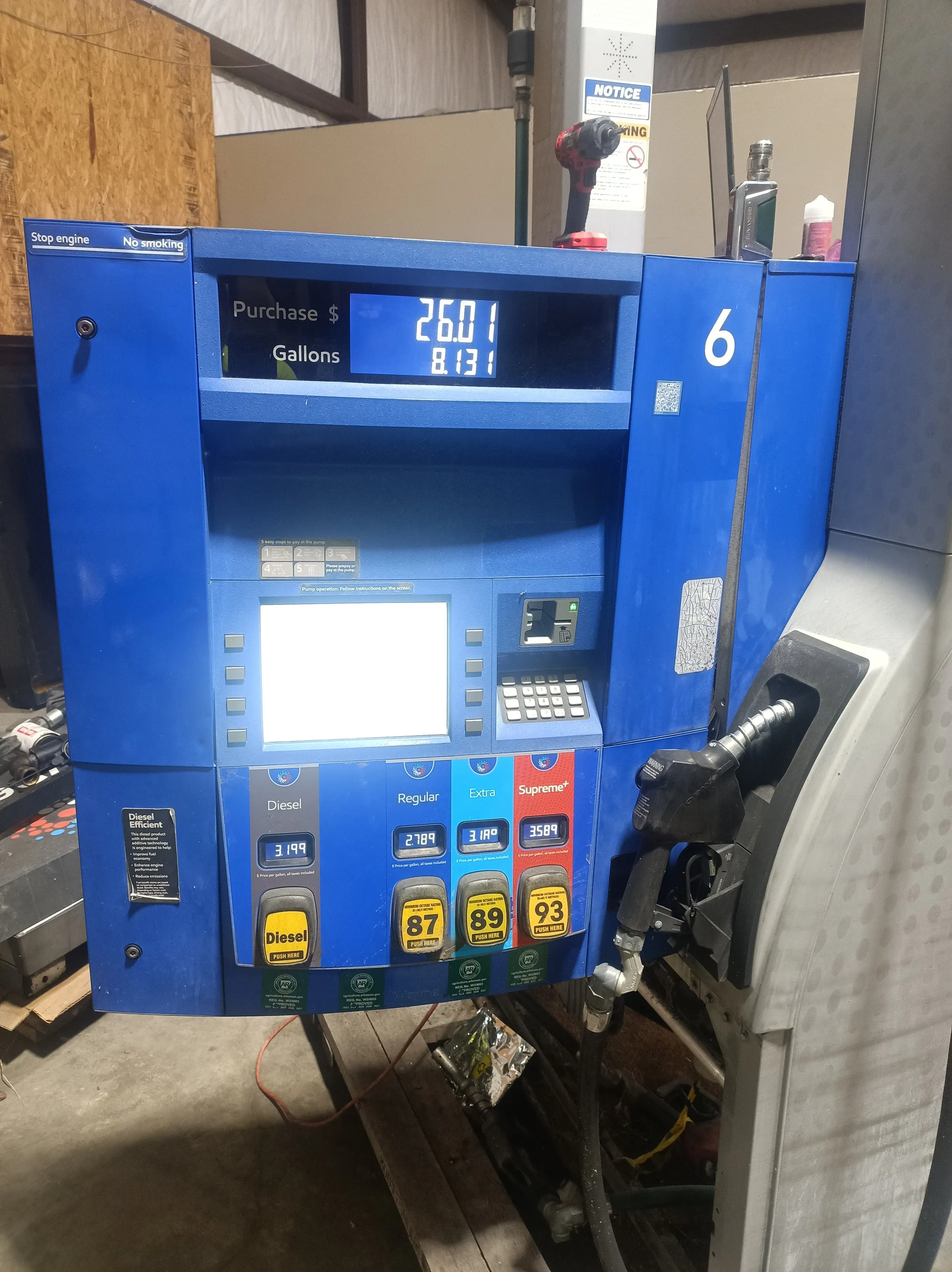 A blue fuel dispenser in the workshop for refurbishment, its price and gallon display lit and grade selectors visible.